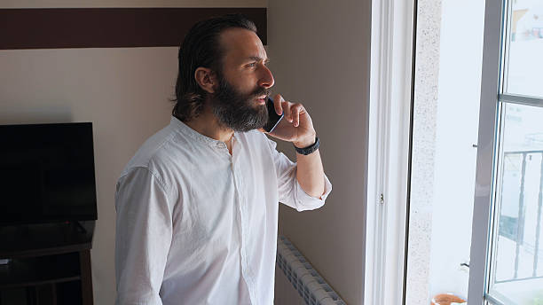 istock Confident Bearded Man Talking on Smartphone Near a Window 2210465114