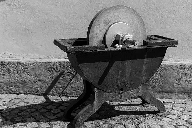 A senior man grinds and cuts metal pipes on a grinding machine in the yard of his house, dressed in old and dirty clothes. Real life.