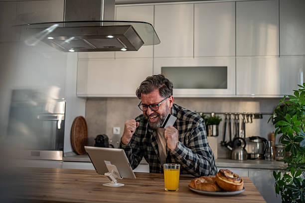 istock Excited mature man making online payment with credit card in kitchen 2210467886