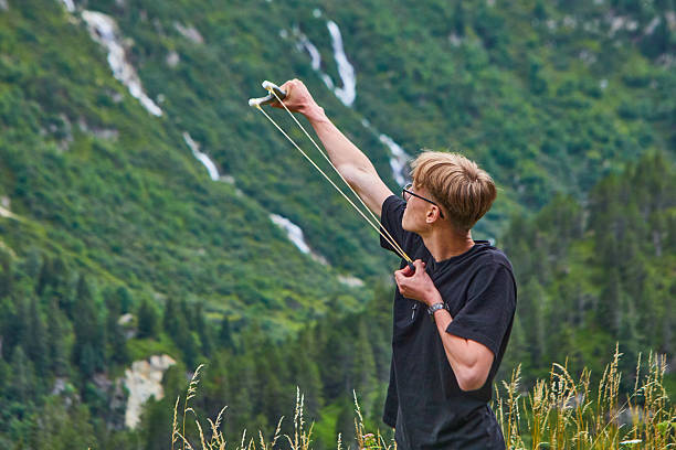 A person demonstrates slingshot skills in an outdoor mountain setting, amidst lush greenery and rugged terrain, perfectly capturing the spirit of adventure and nature's tranquility.