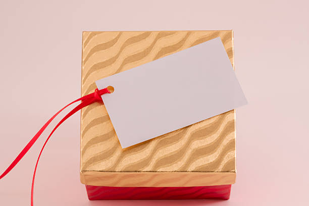 Overhead view of gift box with blank white gift tag and red ribbon on gold wavy patterned lid with red wavy patterned base.