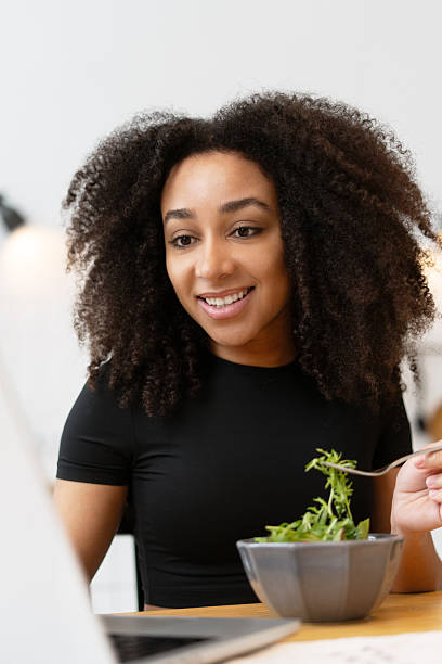 istock Young woman eating salad while working on laptop 2210495152