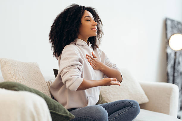 istock Young woman practicing breathing exercises sitting on sofa at home 2210495203