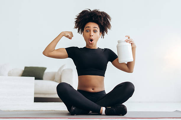 Young woman showing muscles and holding nutritional supplement after workout