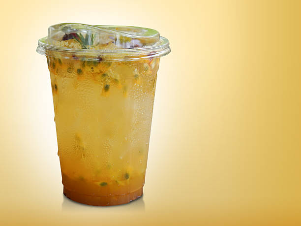 fresh yellow passion fruit in a clear plastic glass. Decorated with flowers and leaves on gradient yellow background, fruit, nature, drink, fresh, copy space