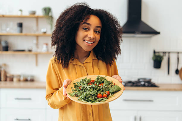 istock Young woman holding wooden plate with fresh salad inside modern kitchen 2210502021