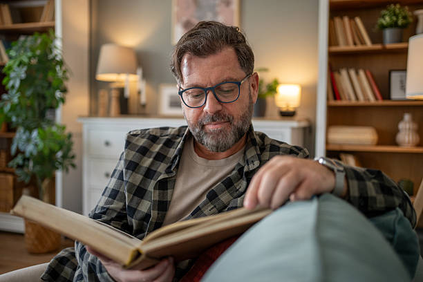 istock Mature man reading a book at home on the sofa 2210503248