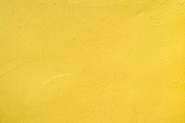 Full frame close-up of a bright yellow painted wall with subtle imperfections and texture, ideal as a colorful background.