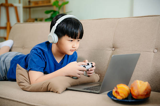 istock Mother and son sitting together on the couch playing computer game in room 2210507402