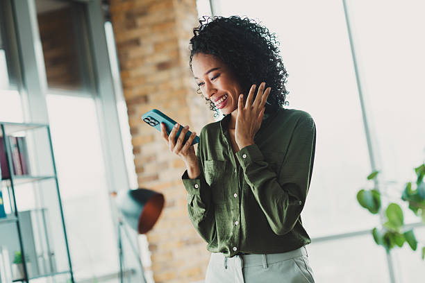 istock Young professional woman smiling while using smartphone in a bright modern office setting with natural light and stylish decor 2210507835