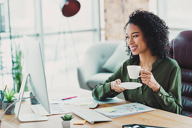 istock Young confident professional woman enjoying coffee while working in a modern office with natural light and stylish design 2210507851