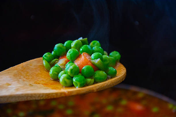 Green peas with carrot cooking in a pot. A wooden spoonful of delicious green peas. Healthy eating.