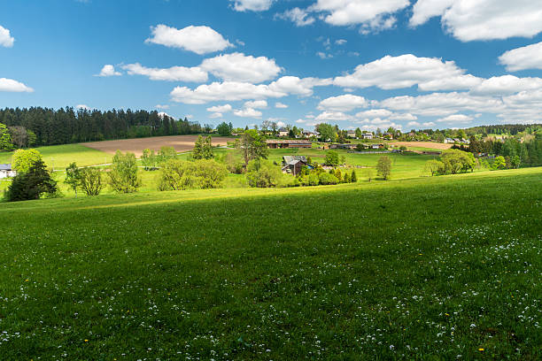 Springtime hilly countryside above Markneukirchen town in Germany with disepersed settlement, flowering meadows, fields and blue sky with clouds