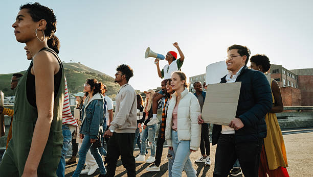 A mixed group of individuals participating in a public protest, holding signs and chanting to express shared beliefs in an outdoor city setting during daytime.