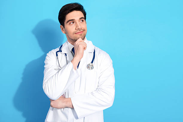 istock Young male doctor in a white uniform contemplating with a thoughtful expression against a blue background 2210518679