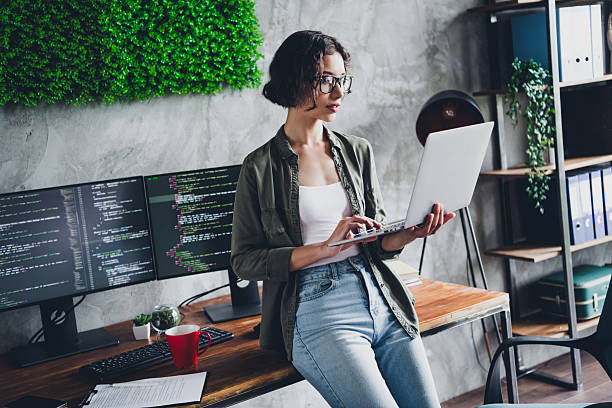 istock Young female programmer working on a laptop at home office surrounded by coding screens in a casual creative workspace 2210519324