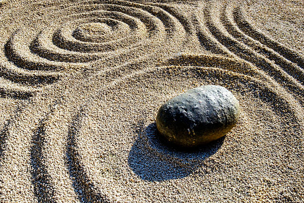 Intricate patterns formed in fine sand create a tranquil atmosphere, with a prominent stone at the center, reflecting the peaceful essence of a zen garden.