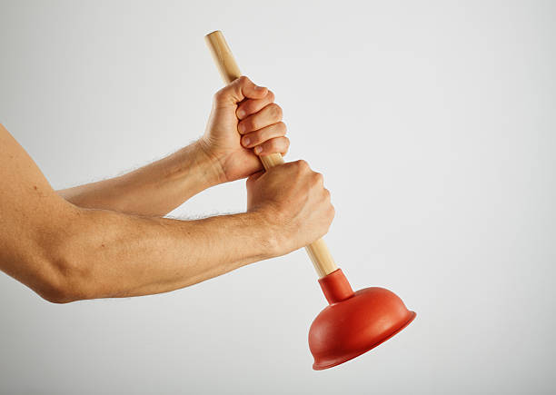 Hand holding a red rubber plunger with wooden handle on white background