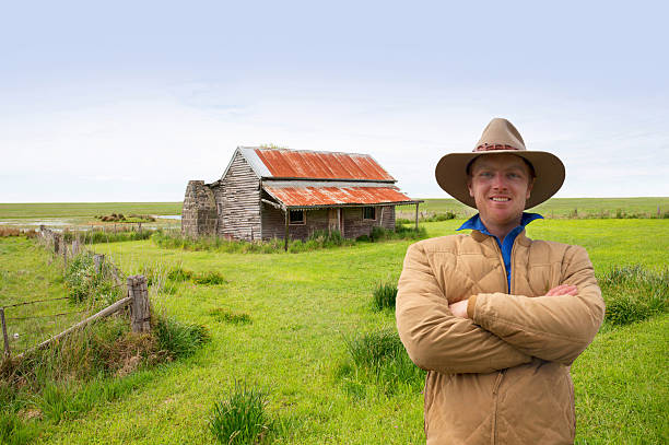 Portrait of a farmer standing in a field with a barn in the background, looking at the camera, serious and confident. He is a senior man in his 60s.