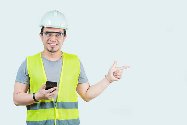 istock Handsome architect holding phone pointing at blank space isolated. Smiling young engineer holding smartphone and pointing at a blank space isolated 2210527250