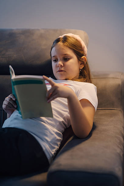 istock Young girl reading a book while relaxing on sofa 2210527487