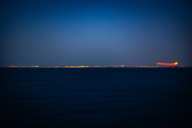 Artistic background created by long exposure camera movement over the horizon where the sea meets the land, featuring vibrant city lights.