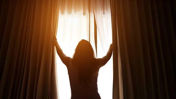 istock Woman opening curtains in hotel room letting light in 2210530077