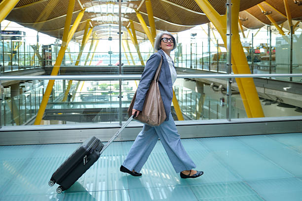 istock Senior businesswoman walking in airport terminal pulling suitcase 2210534079