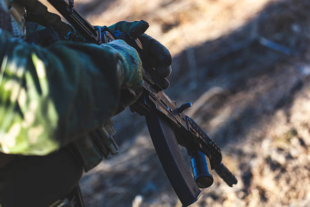 istock Camouflaged soldier gripping rifle during intense airsoft combat, displaying tactical awareness and preparedness 2210534476