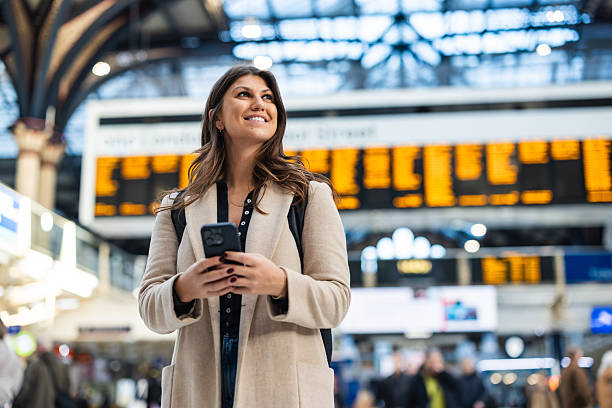 istock Young woman checking train schedule on smartphone in busy station 2210534512