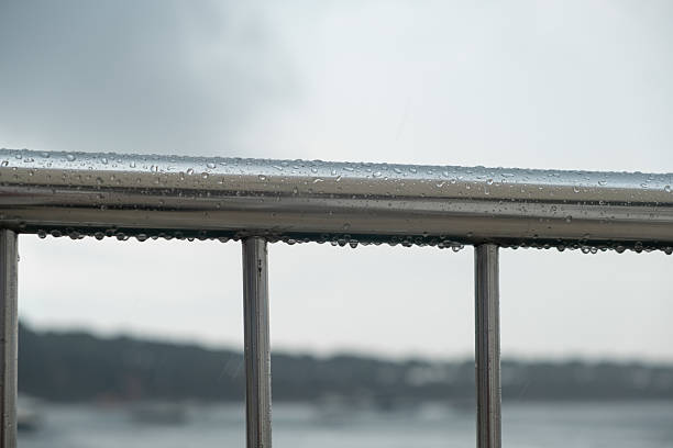Metal railing glistens with rain drops as a cloudy sky looms over the Bosphorus, capturing the essence of a typical Istanbul day on the water.