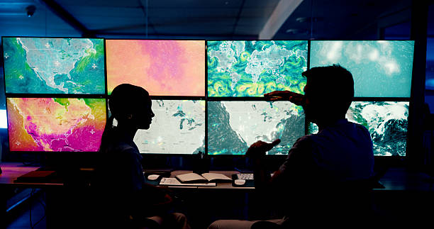 istock Computer, screen and maps with people in control room for storm tracking, satellite forecast or planning weather pattern. Back, meteorology team or radar data for climate monitor, silhouette or night 2210543351