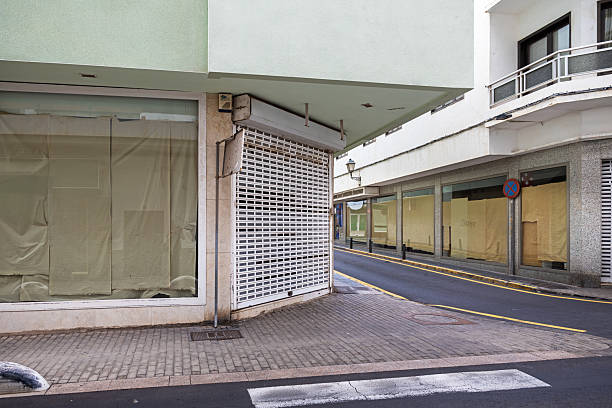 This image captures a row of closed storefronts, their windows covered with brown paper, signaling renovation, relocation, or business closure. The quiet street, devoid of pedestrians, adds to the atmosphere of uncertainty and transformation. The muted tones of the paper contrast with the surrounding architecture, emphasizing the temporary nature of change in urban spaces. The picture is taken in Arrecife which is the main city on the Canary Island Lanzarote
