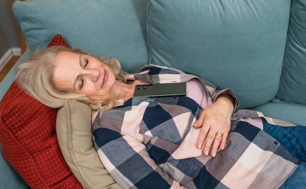 istock Senior woman sleeping peacefully on sofa with smartphone on chest 2210544320