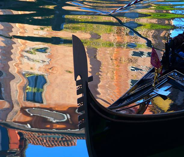 Gondola Ferri and Water Reflections Close-up - Detailed close-up of a gondola's metal ferri (bow)** **and the abstract, shimmering reflections of canal-side buildings on the water.