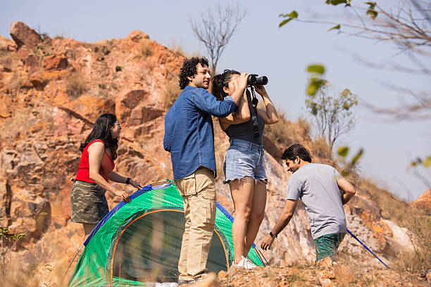 istock Young man looking away and showing something to female friend holding binoculars while camping together on rocky mountain during sunny adventure 2210546255