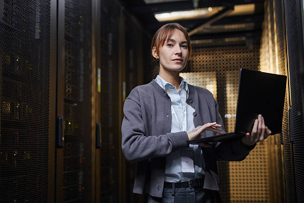 istock Woman Working on Laptop in Server Room Surrounded by Equipment 2210548494