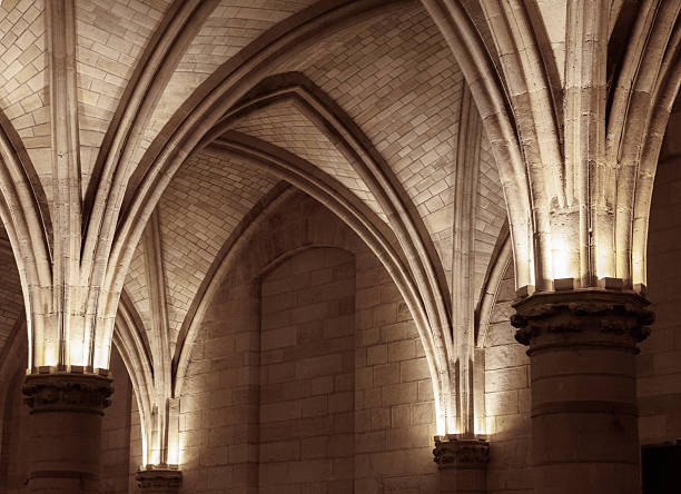Gothic ribbed vaulting and stone arches inside the Abbey of Mont Saint-Michel. Historic Gothic vaults and textured stone walls illuminated in Mont Saint-Michel’s interior.