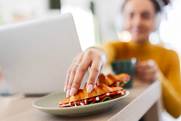 Woman eating sandwich while working on laptop