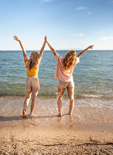 Redhead senior mother and her adult daughter are walking together on the sea shore. Happy loving mom and her grown up child embracing and admiring of nature.