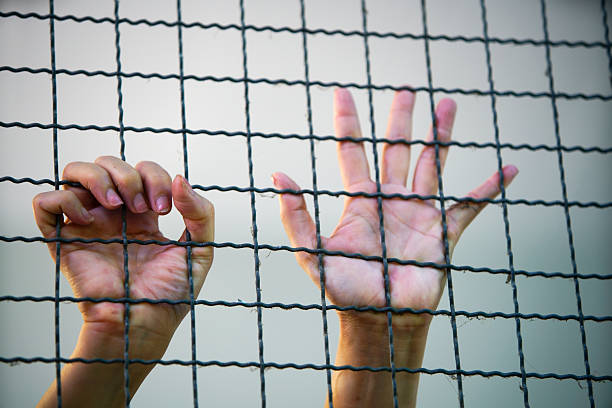istock Hands Grasping Metal Bars in a Confinement or Captivity Setting 2210551829