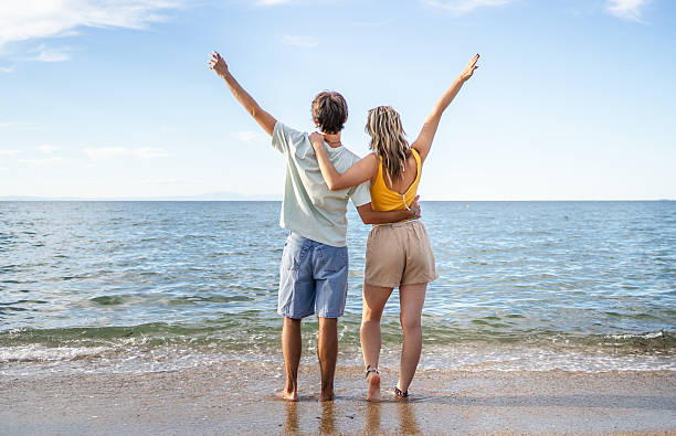 istock Young couple embracing and raising arms on beach 2210552229