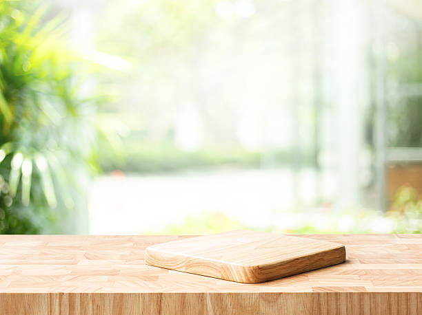 istock Wooden cutting board placed on a textured wooden countertop, with soft sunlight streaming through house wall area  and blurred green landscape in the background.cooking, kitchen decor, 2210554564