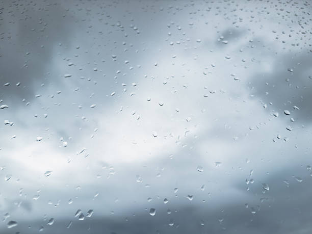 Raindrops on a window with a view of dark gray clouds with a blue cold tint. High quality photo