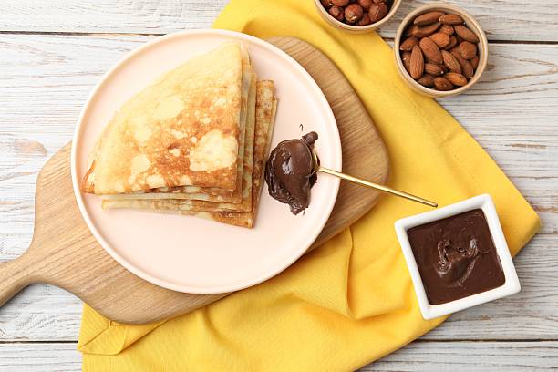 istock Delicious crepes with chocolate paste and nuts on wooden table, flat lay 2210570209
