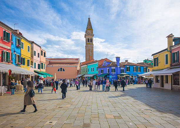 Venice, Italy - 13 March 2025 - Burano, the town of a thousand colors, an enchanted colorated buildings island in the heart of the Venice sea lagoon, here a view during the winter with tourists in the central square.