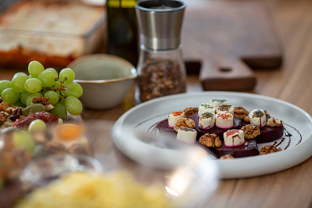 A close-up view of a beautifully plated beetroot and goat cheese dish garnished with herbs and walnuts, surrounded by fresh grapes and culinary elements in a cozy dining setting set against rustic wooden table in warm, diffused lighting.