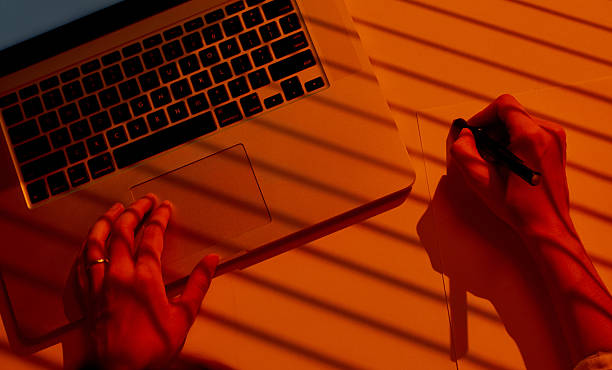 istock Female Hands Drawing on Paper beside Laptop with Dramatic Light. 2210574046