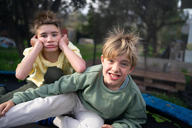 Two young boys, cousins like brothers, stand close together, looking directly at the camera with friendly smiles. One wears a yellow shirt, and the other wears a pale blue shirt. Their bond is evident in their relaxed and happy expressions, captured in a natural outdoor setting.
