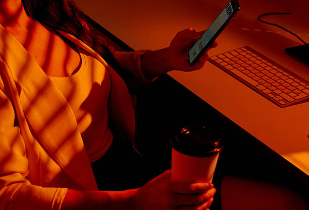 istock Woman Browsing Phone with Coffee at Desk in Warm Office Light. 2210575484